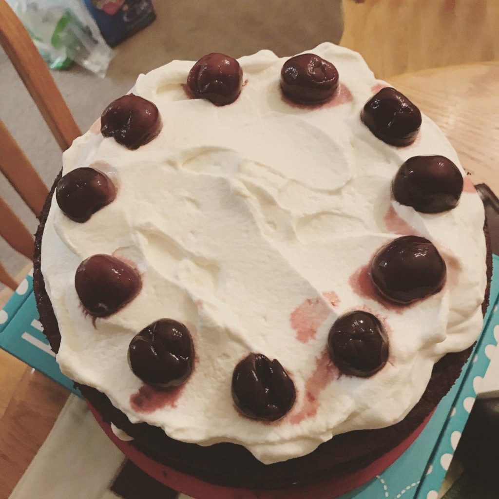 A round cake covered in whipped cream and cherries.