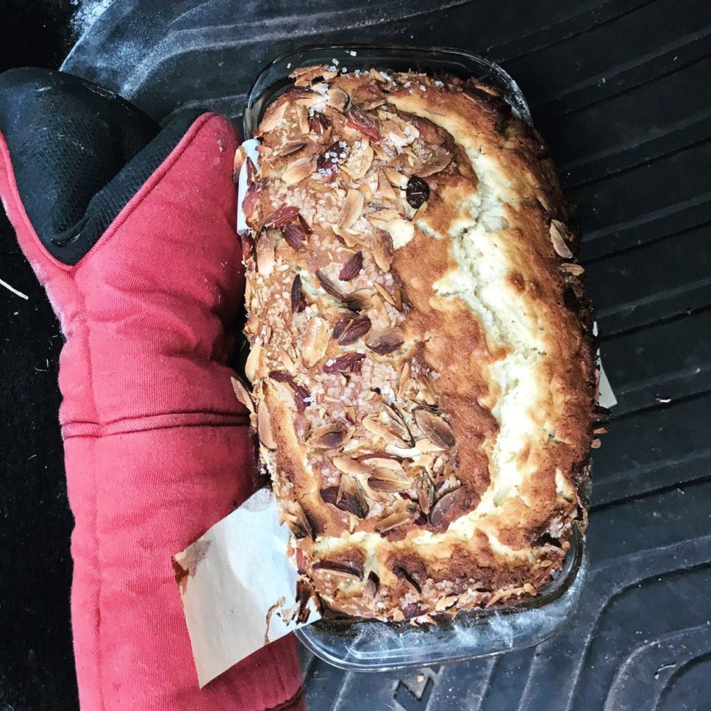 A brown cake in a loaf pan next to an oven mitt. 